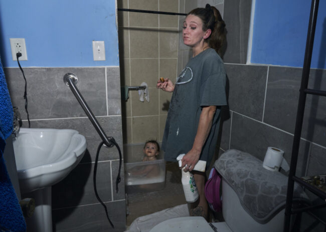 Mayron Hollis grabs a bit to eat while she bathes her daughter, Zooey, and cleans the bathroom.