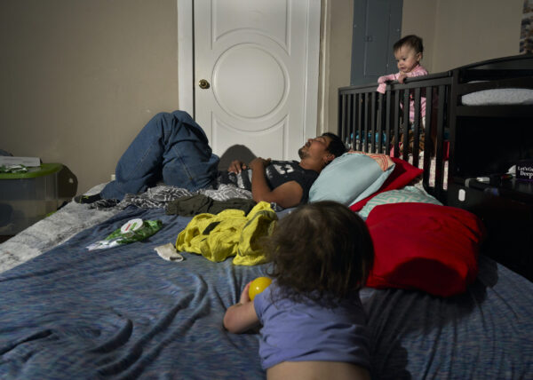 Chris Hollis napping as his two young daughters, Zooey and Elayna, play nearby.