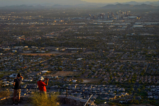 A hiker on a bluff takes photographs of the sprawl of Phoenix