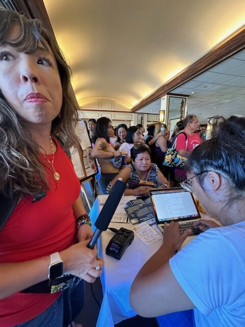 Freelance journalist Erika Hayasaki holds recording equipment as she covers the aftermath of the August 2023 Maui wildfires. In this photo, several residents displaced by the fire came to a center to seek financial and housing assistance.