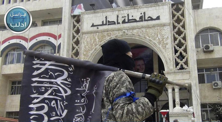 In this photo posted on the Twitter page of Syria's Al Qaeda-linked Nusra Front in 2015, a fighter holds his group flag as he stands in front of the governor building in Idlib province in northern Syria. 