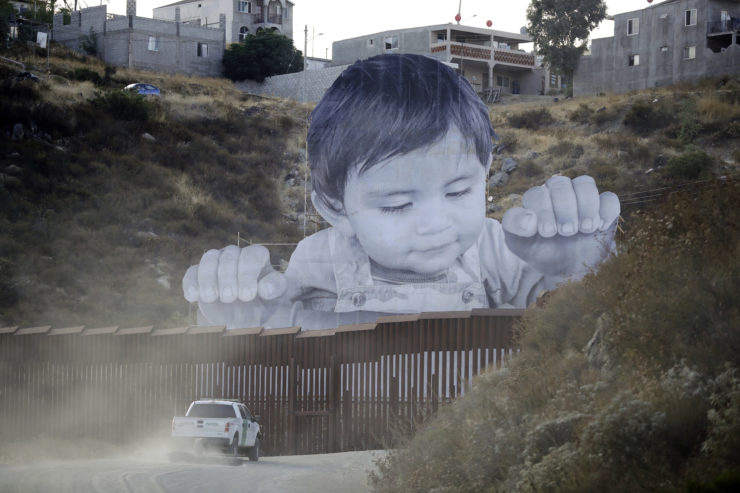 A Border Patrol vehicle drives in front of a mural in Tecate, Mexico, just beyond a border structure in Tecate, Calif.