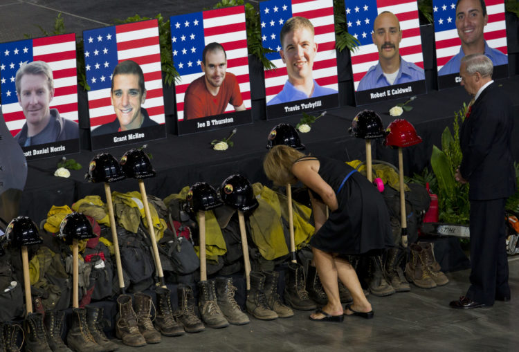 Memorial service for 19 fallen wildlands firefighters, showing their helmets and boots with firefighting tools.