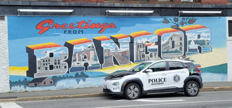Police car from Bangor, Maine, in front of a billboard advertising the city.