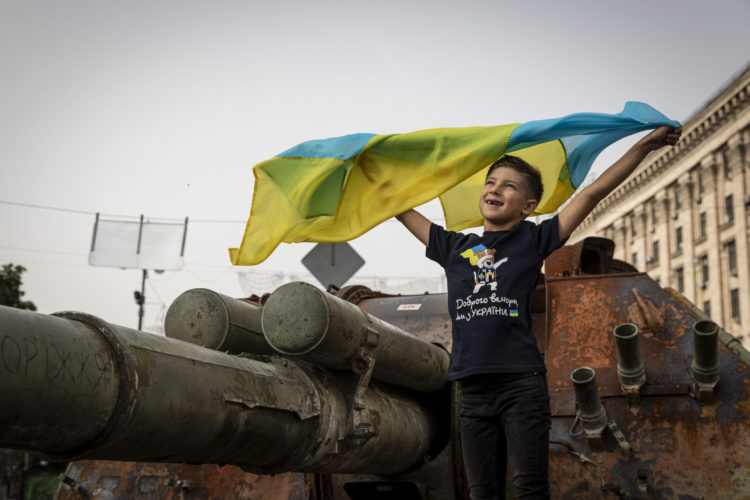 A boy in Kyiv waving a Ukrainian flag over destroyed Russian tanks
