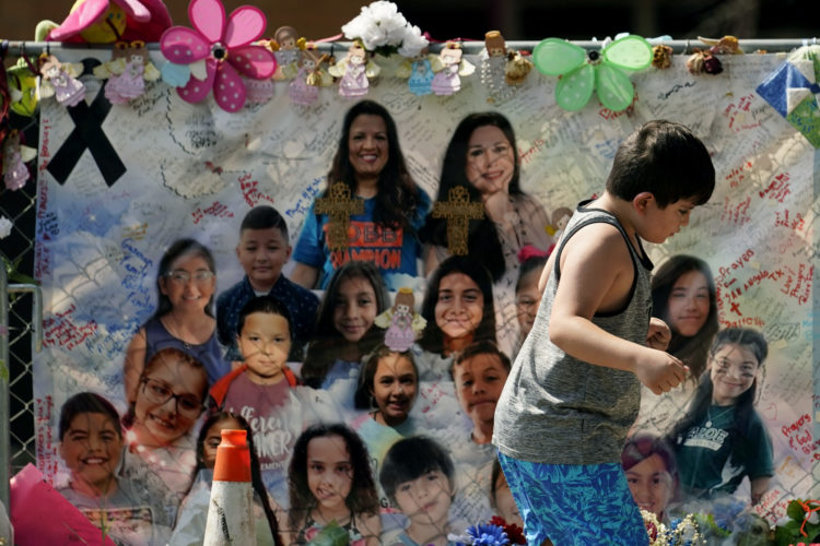 Photo of a young boy walking in front of a mural of students and teachers killed in the May 2022 shooting at Robb Elementary School in Uvalde, Texas.