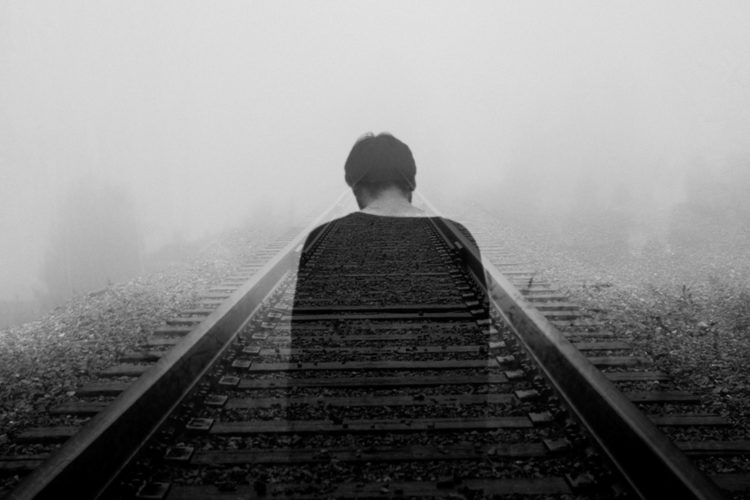 Photograph of a man standing in the haze on a train track.