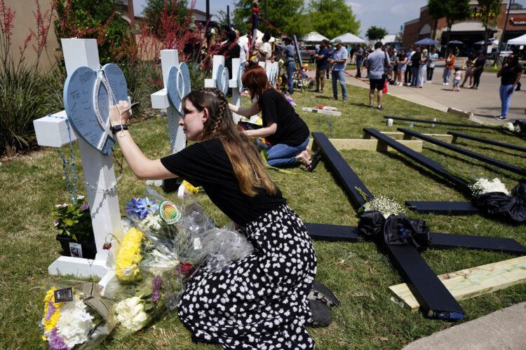 Photo fo a woman woman signing a makeshift memorial cross after a May 6, 2023, mass shooting at a mall in Allen, Texas