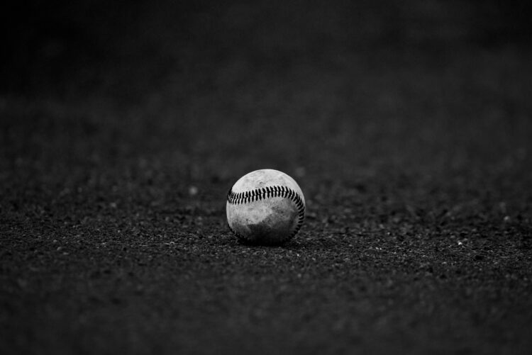 A black-and-white photo of a baseball sitting alone on a field