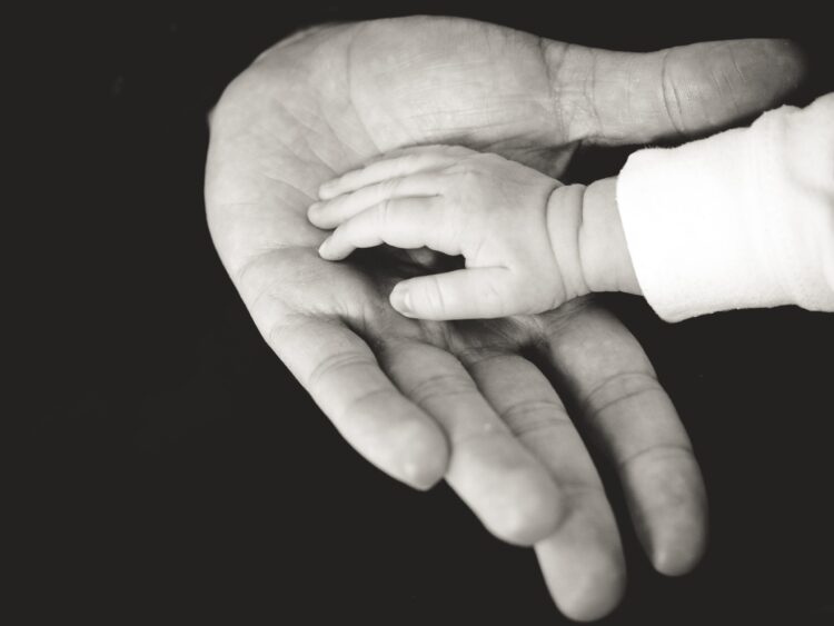 Black-and-white photo of a baby's hand in a father's hand.