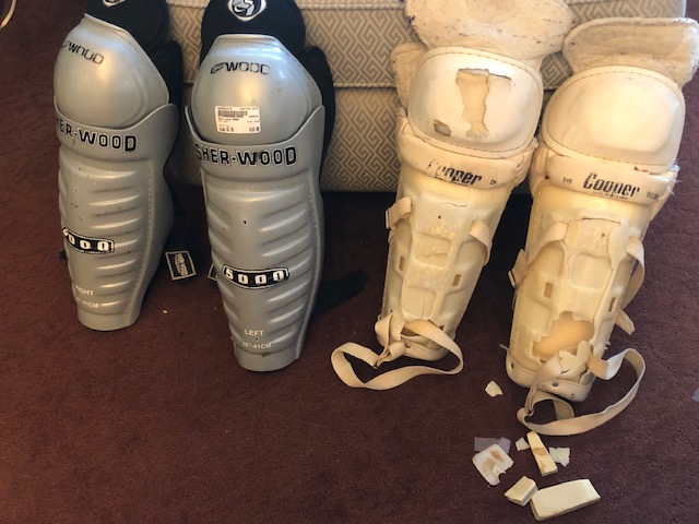 Hockey shin guards, one new and shiny-silver, one old, white, battered and broken.