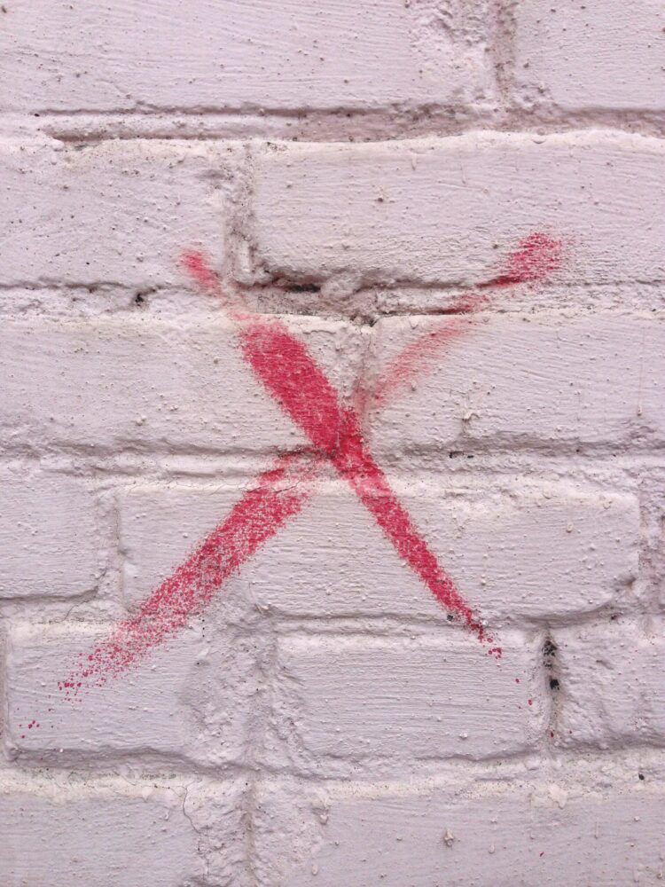 White brick wall painted with a red X.