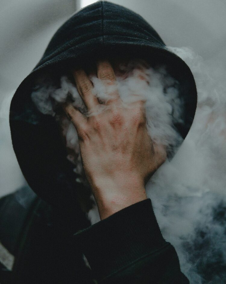 Photo of a man in a hoodie with his face obscured by smoke