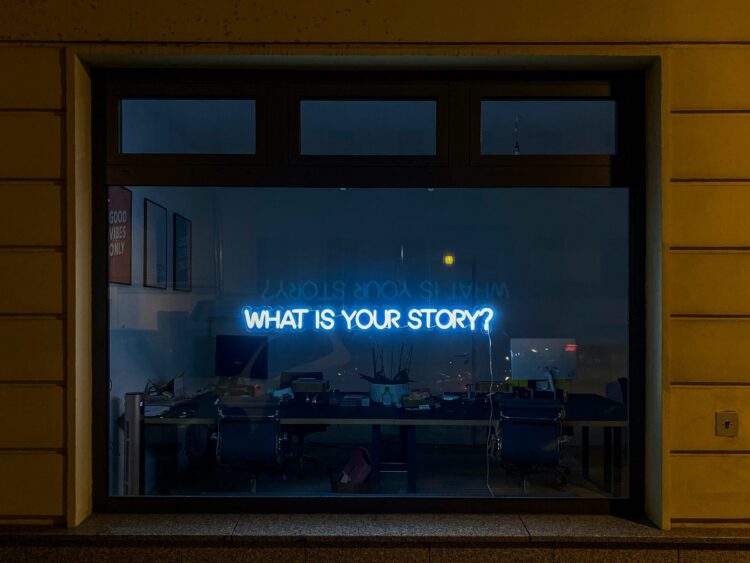 Neon sign in window that reads WHAT IS YUOUR STORY?
