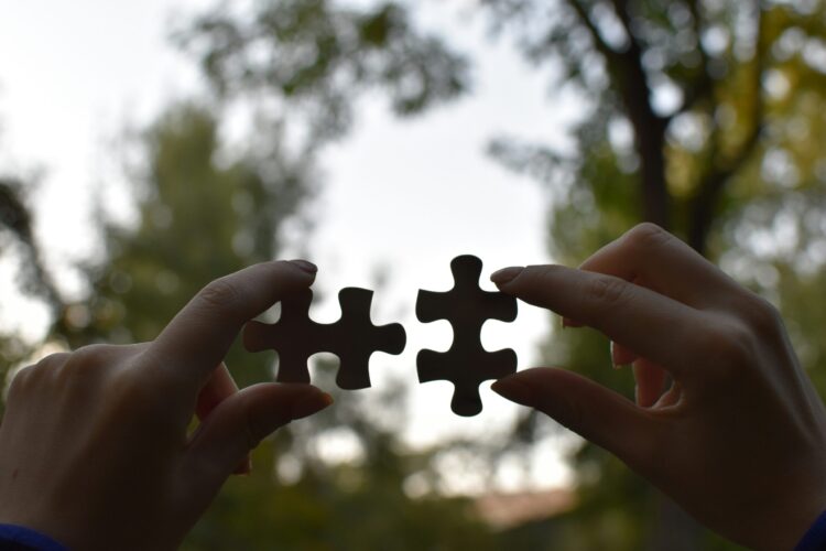 Photo of two hands holding jigsaw puzzle pieces that fit together.