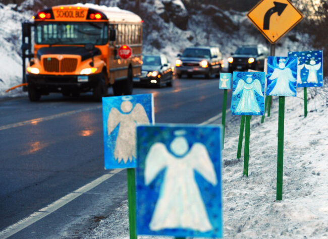 A school bus and several cars drive past posters of angels that line the road to Sandy Hook Elementary School, three weeks after a mass shooting that left 20 students and six school employees dead.